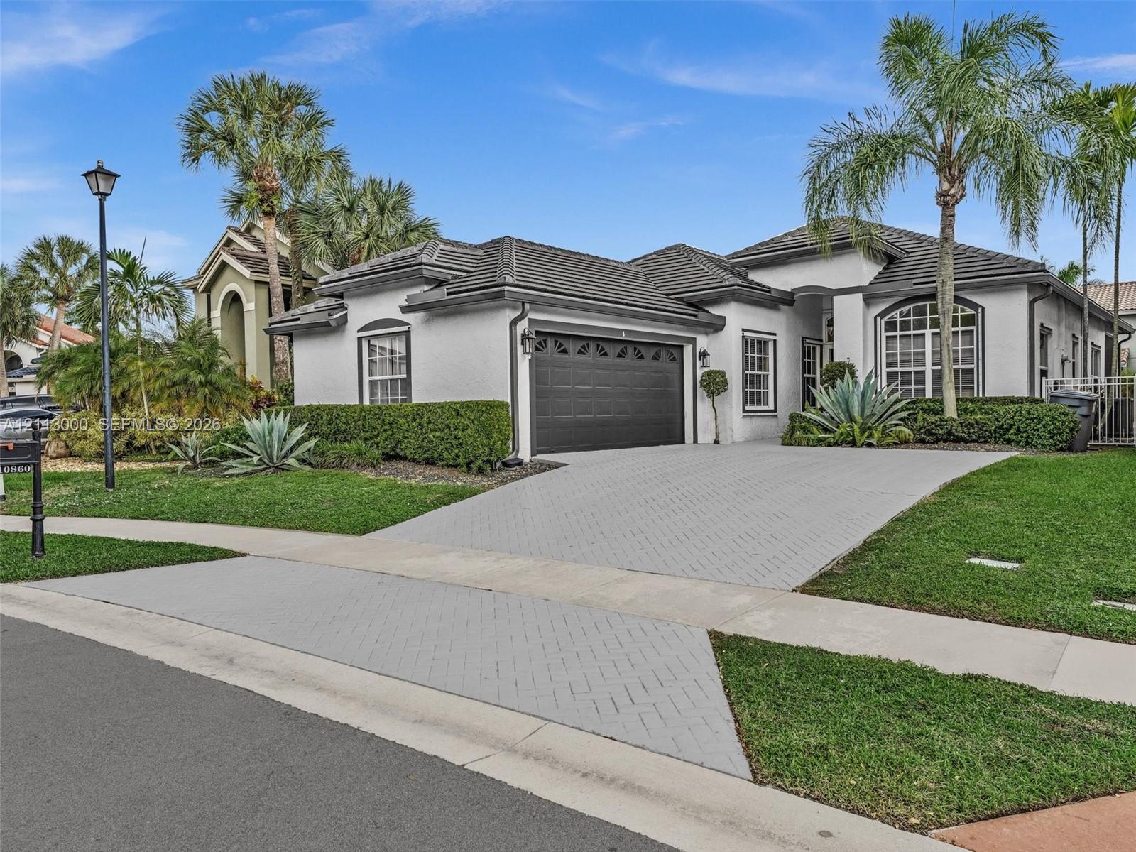 Stucco exterior with a multi-hipped tile roof, decorative arched window accents, and a paved driveway leading to a two-car garage