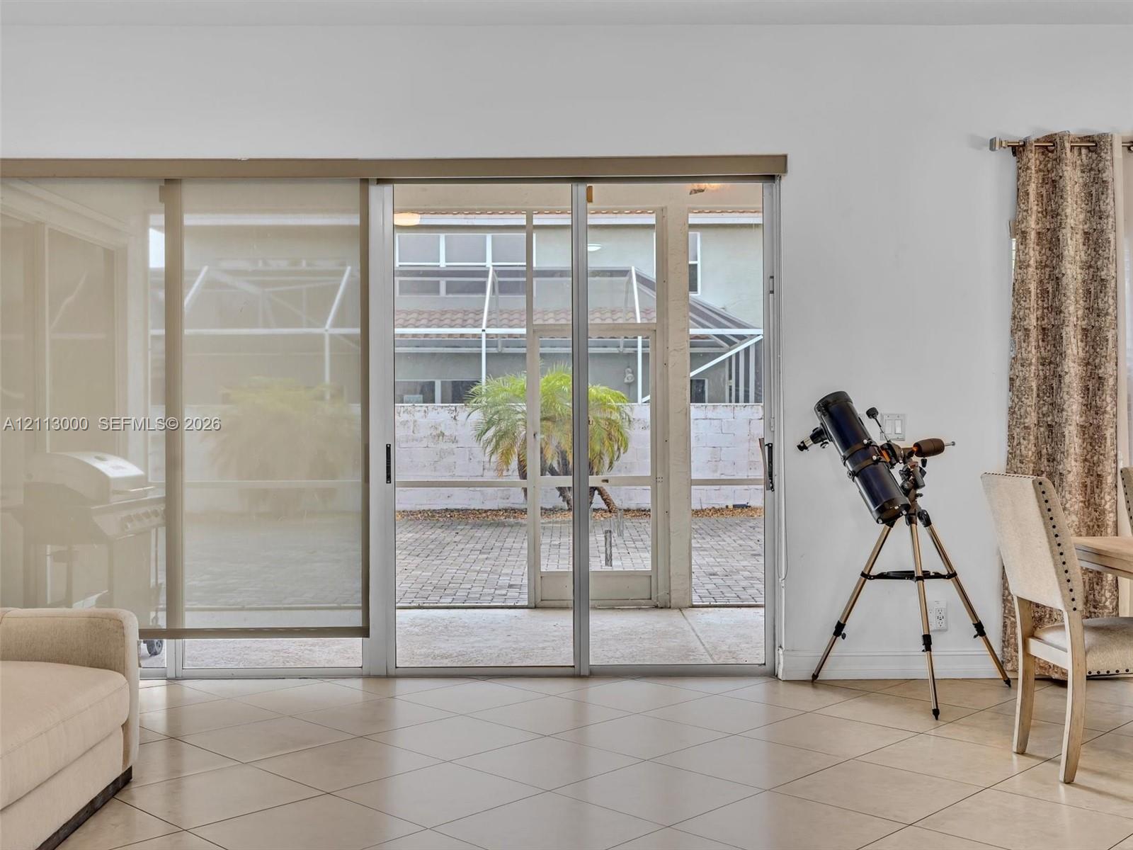 Large-format sliding glass doors with neutral roller shades, ceramic tile flooring, and a screened-in patio featuring paver hardscaping