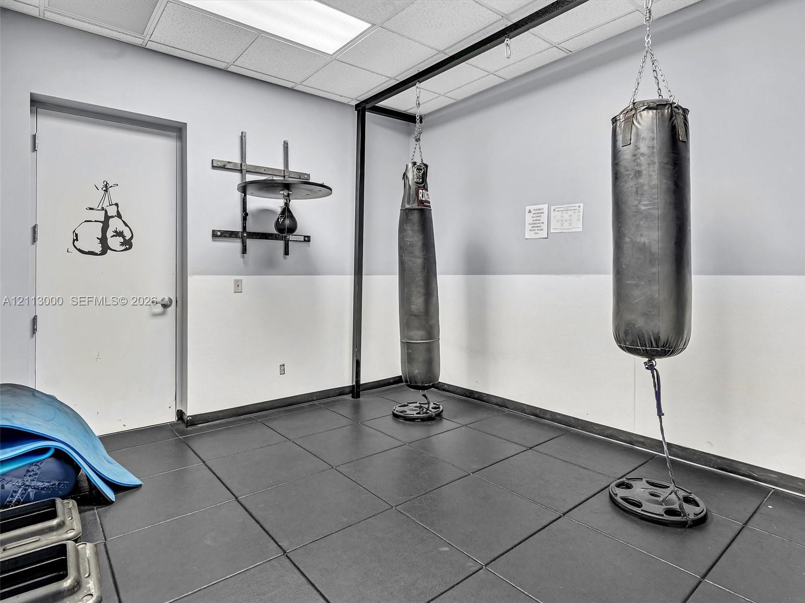 Room featuring rubberized floor tiling, drop ceiling with recessed lighting, and a metal framework support structure