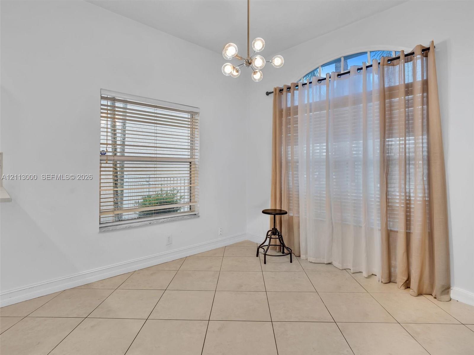 High ceilings featuring a multi-globe chandelier, neutral tile flooring, a large arched window, and rectangular windows with horizontal blinds