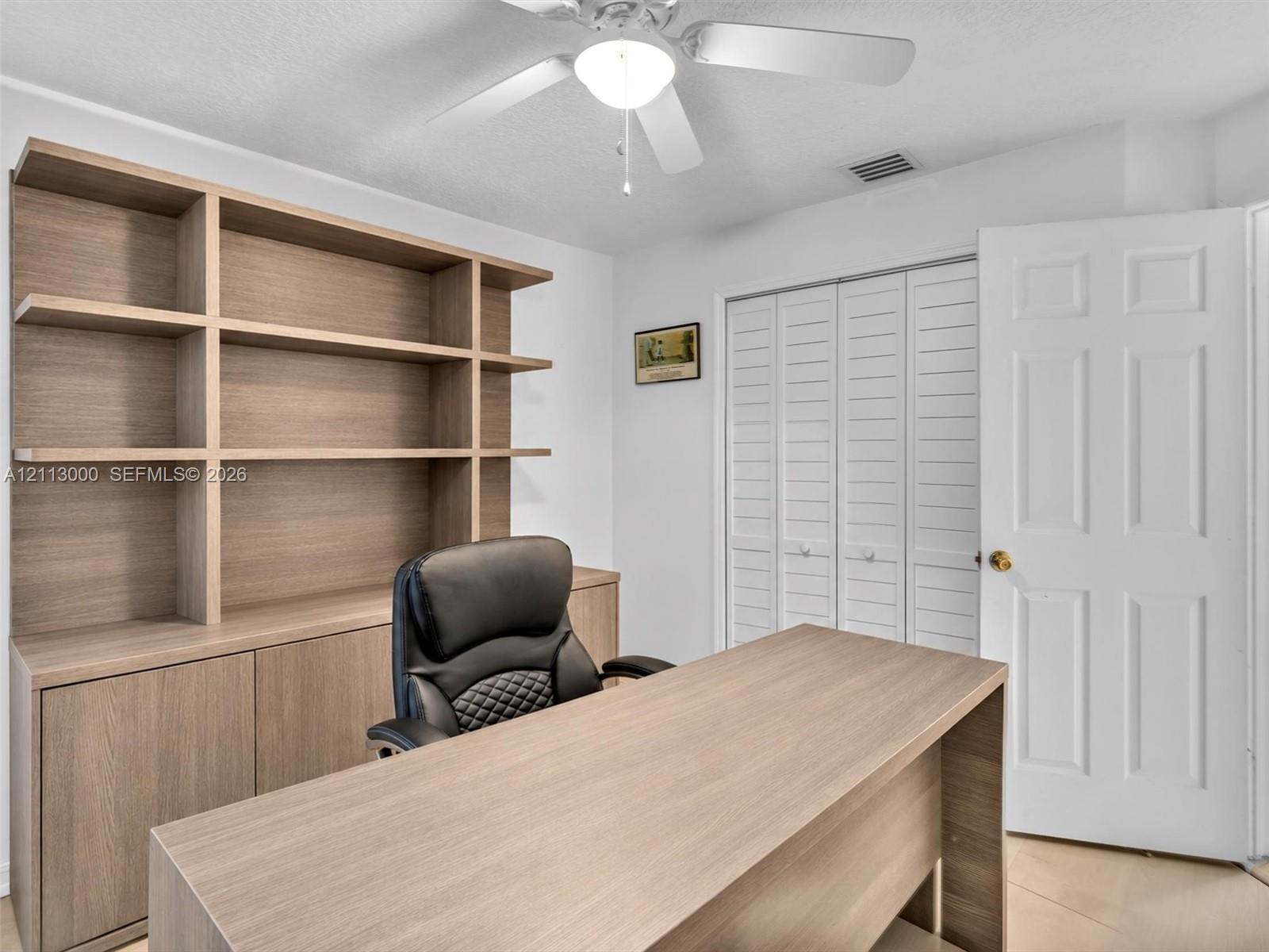 Built-in wood-finish shelving unit, white louvered-style bi-fold closet doors, and ceiling-mounted light fixture