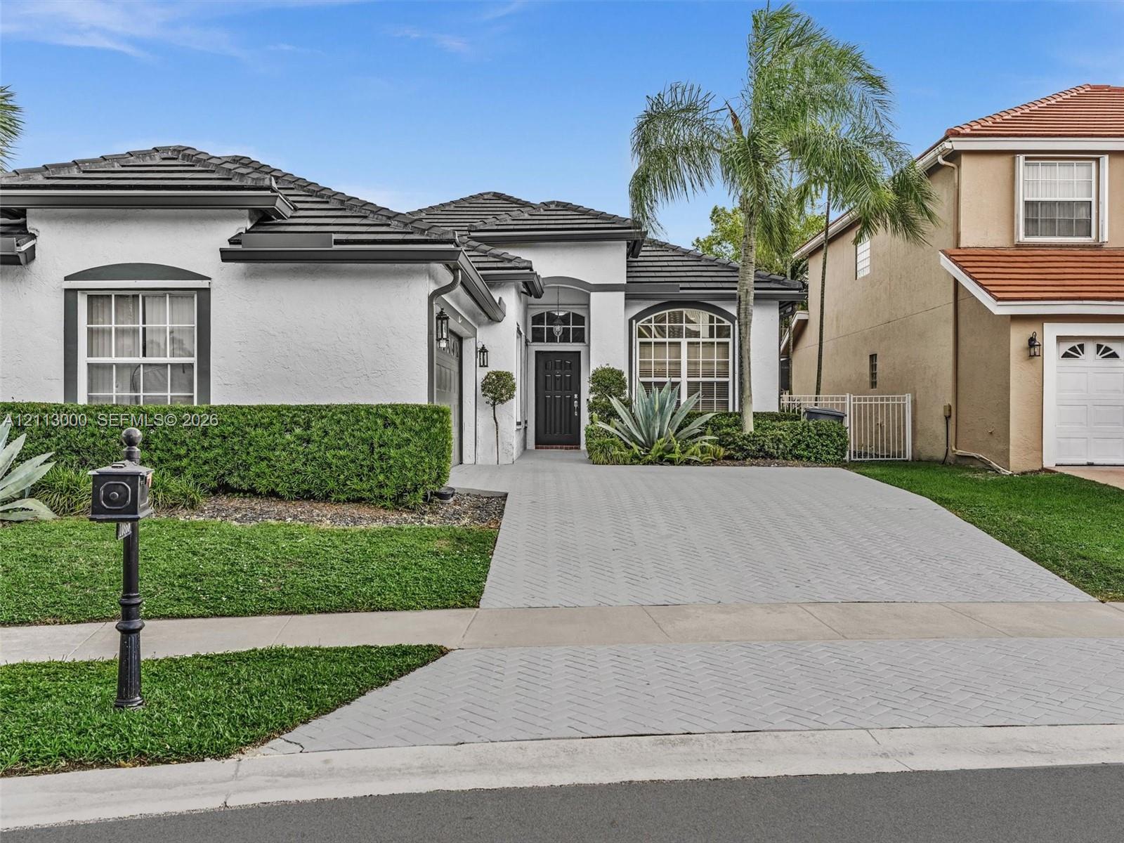 Stucco exterior featuring a dark-toned tile roof, arched entryway, decorative arched windows, and a patterned paved driveway