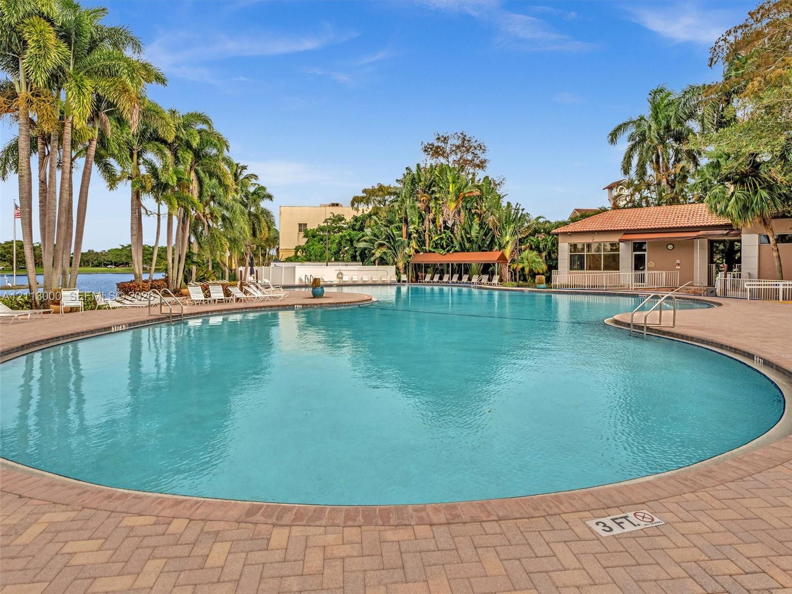 Large community swimming pool with brick paver decking, sheltered seating area, and mature palm landscaping