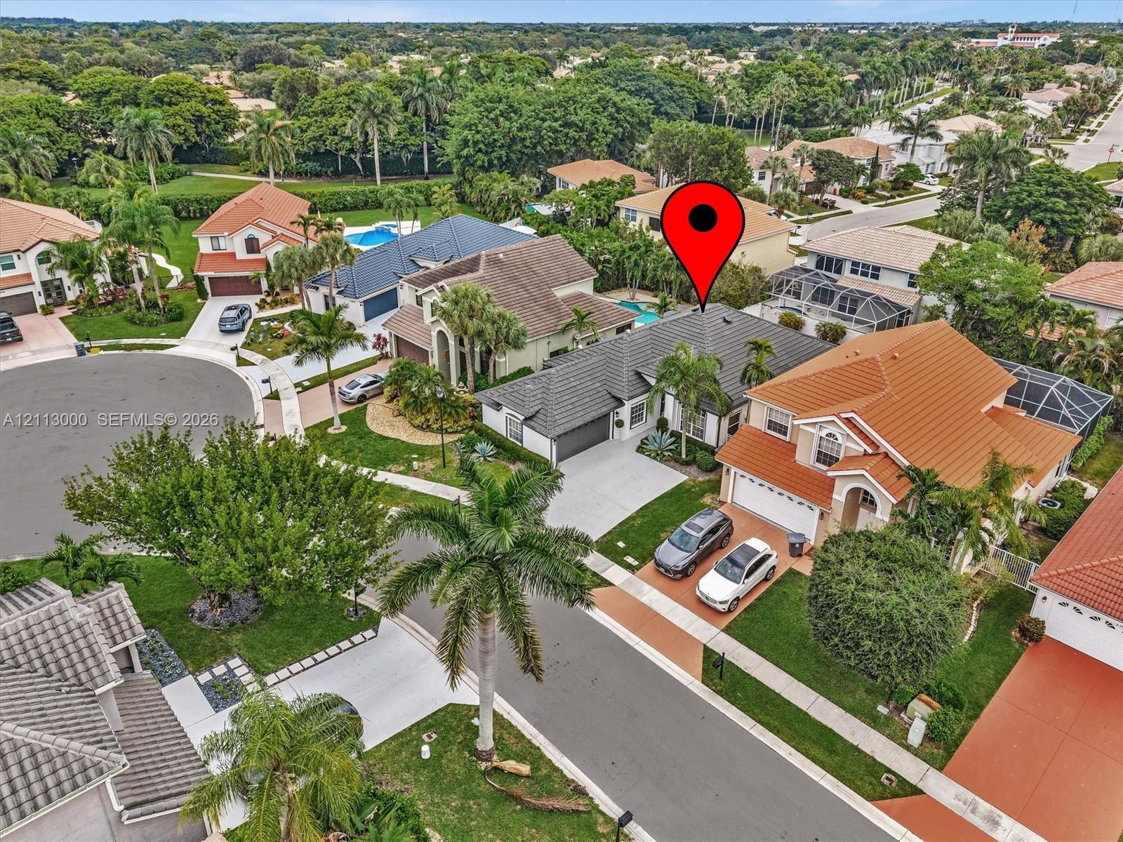 Aerial perspective of a residential property featuring a concrete tile roof, attached multi-car garage, concrete driveway, and established landscaping