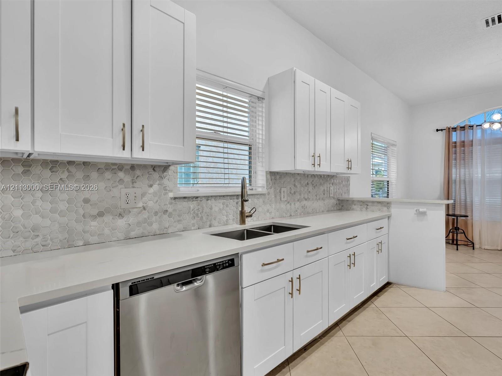 Kitchen featuring white shaker-style cabinetry, a stone hexagonal tile backsplash, quartz countertops, a stainless steel dishwasher, and a gooseneck faucet