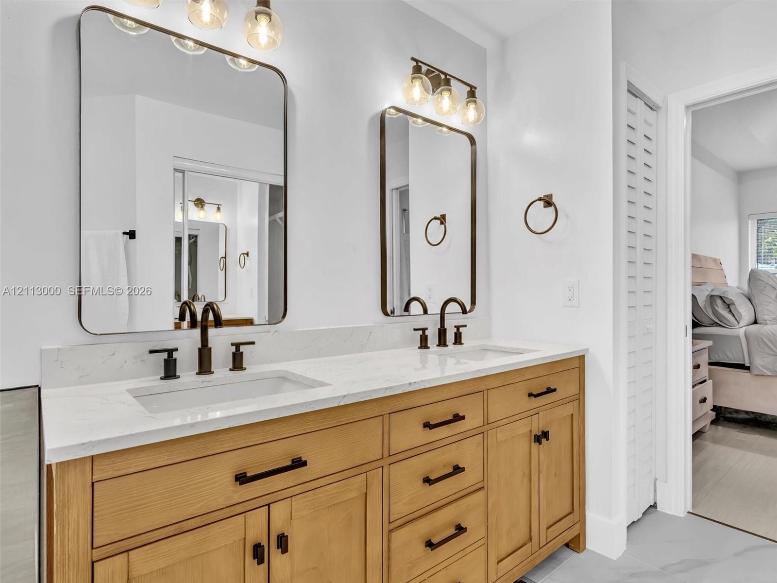 Dual-sink vanity with a light wood-finish cabinet, stone-look countertop, integrated rectangular sinks, oil-rubbed bronze fixtures, and two rectangular wall-mounted mirrors with coordinating light fixtures