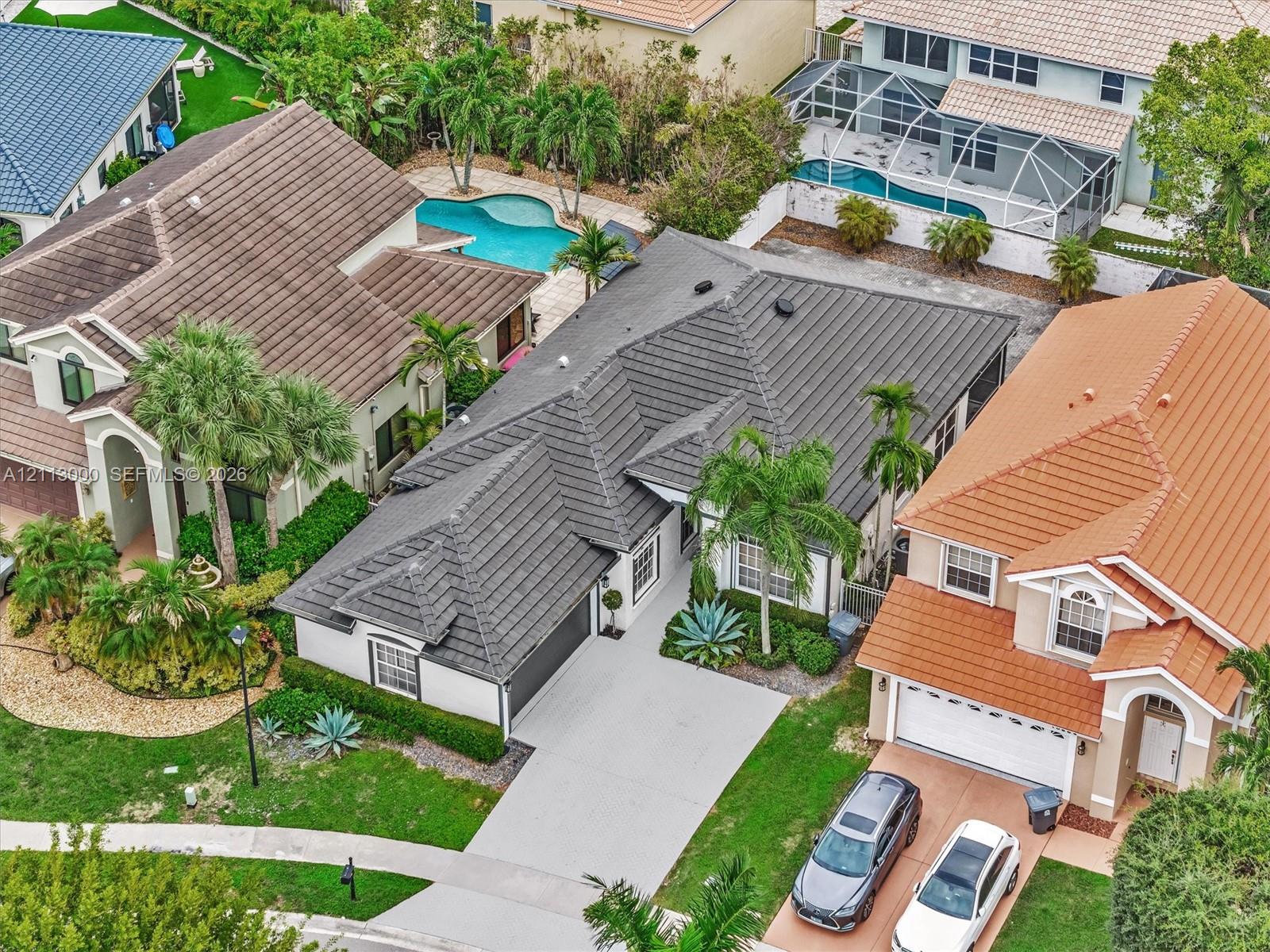 Aerial view of a residential property featuring a dark-toned tile roof, attached two-car garage, concrete driveway, and landscaped front yard