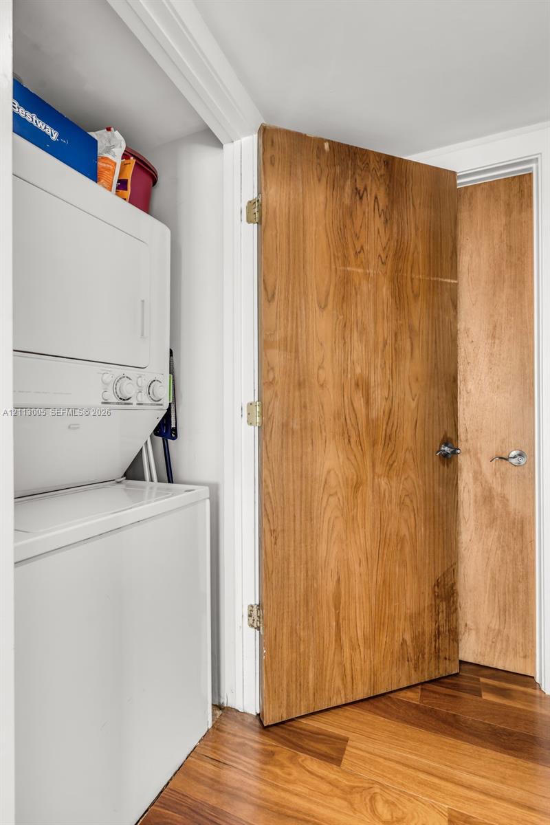 Laundry area featuring a stacked washer and dryer unit, wood-finish flooring, and solid-core wood-finish doors with brushed metal hardware