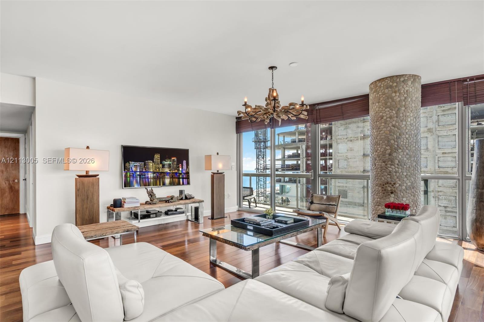 Living area featuring wood-finish flooring, floor-to-ceiling windows, a decorative stone-clad structural column, and a multi-arm chandelier