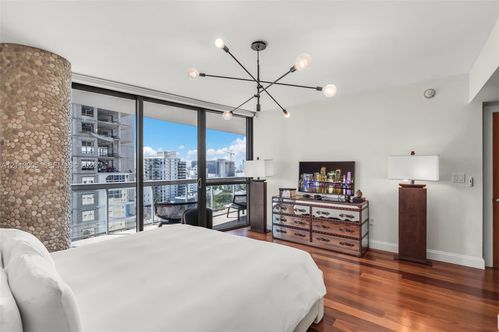 Floor-to-ceiling glass doors, natural stone-clad pillar, wood-finish flooring, and modern multi-arm chandelier