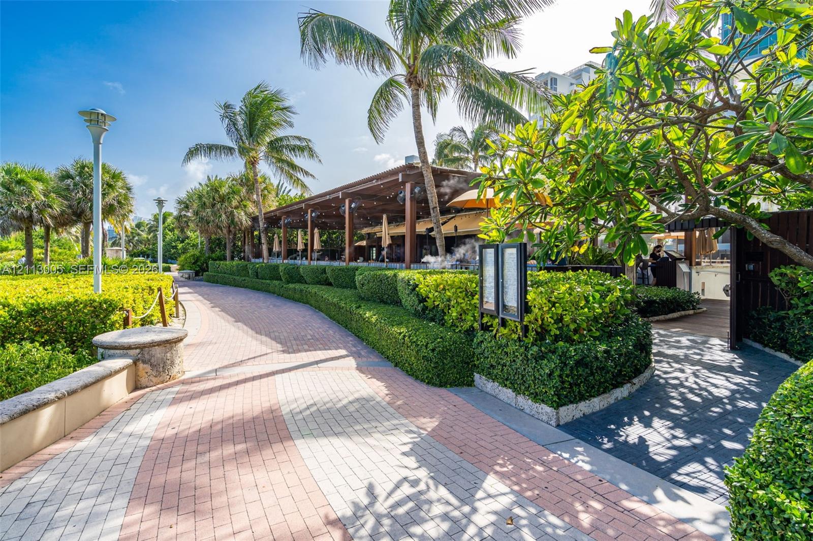 Paver walkway featuring manicured hedges, mature palm trees, and overhead wood pergola structure