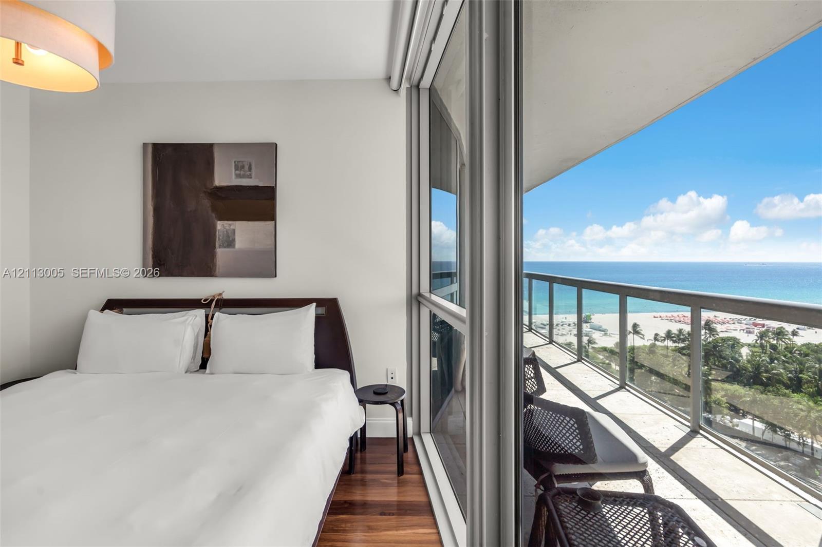 Floor-to-ceiling sliding glass doors, private balcony with metal and glass railing, wood-finish flooring, and recessed ceiling lighting