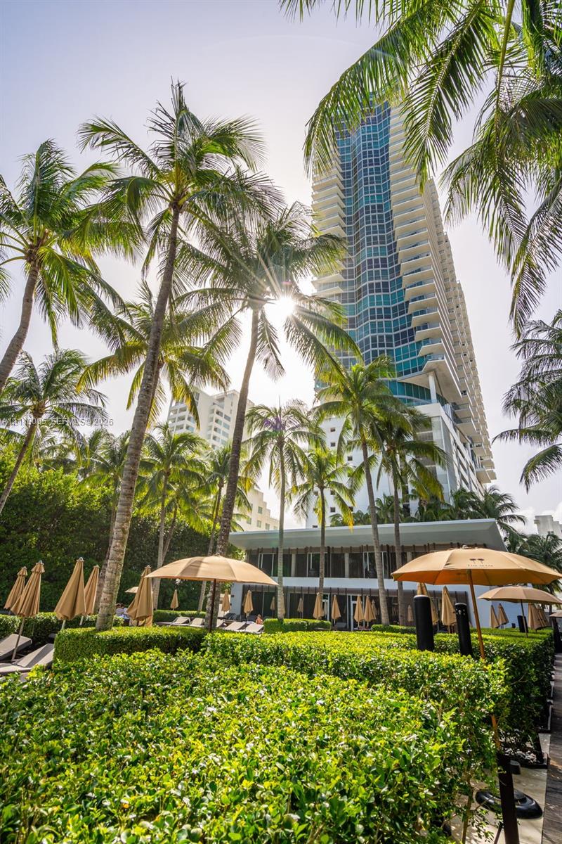 High-rise building with tiered balcony architecture, surrounding palm trees, and manicured green hedges