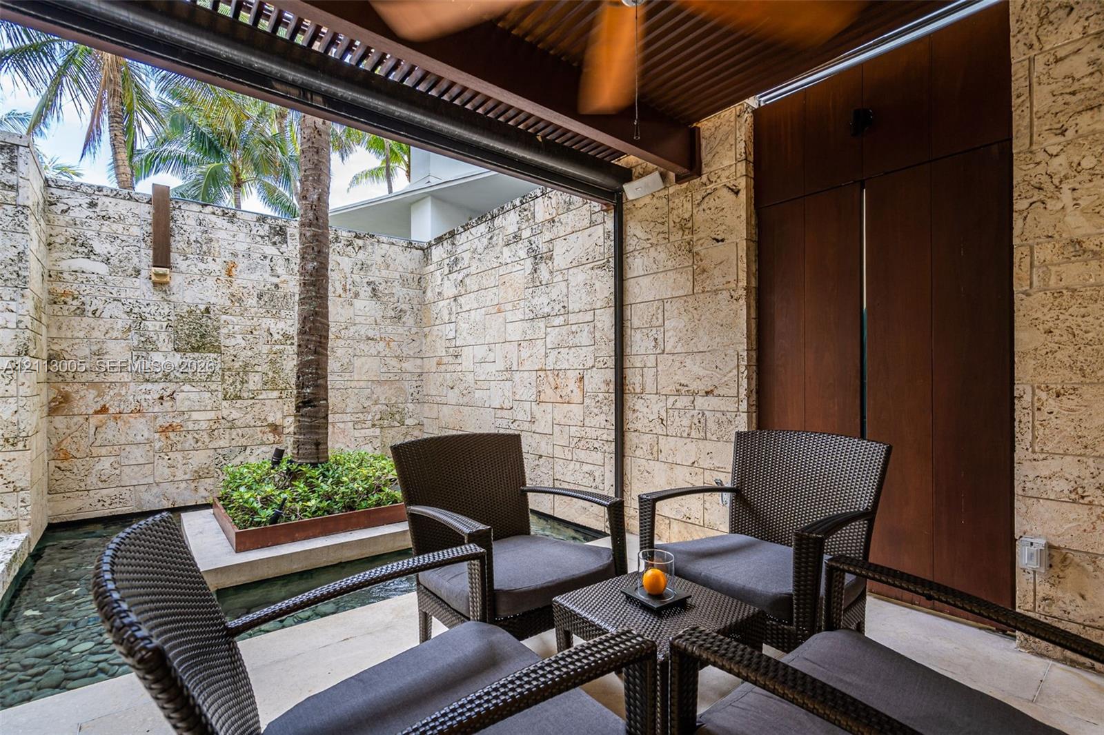 Covered patio featuring stacked stone walls, wood-paneled accents, a coffered ceiling with a mounted fan, and a built-in water feature with a raised garden bed