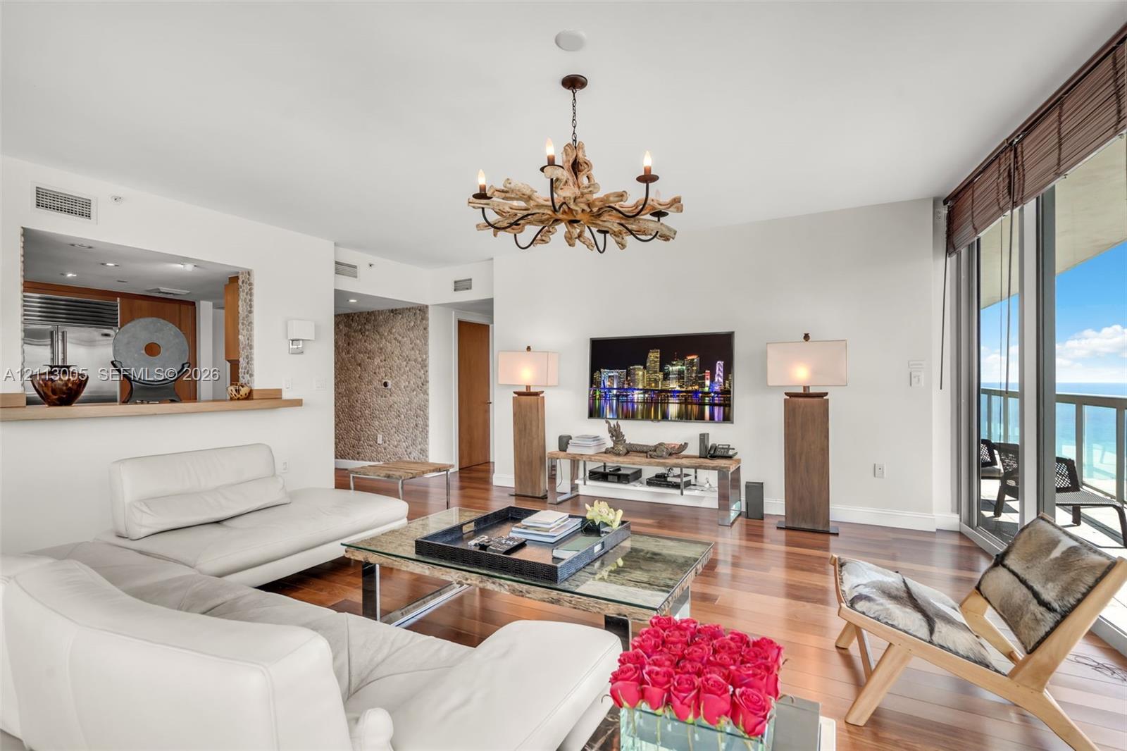 Living area featuring wood-finish flooring, a textured stone feature wall, a custom driftwood-style chandelier, and floor-to-ceiling windows with balcony access