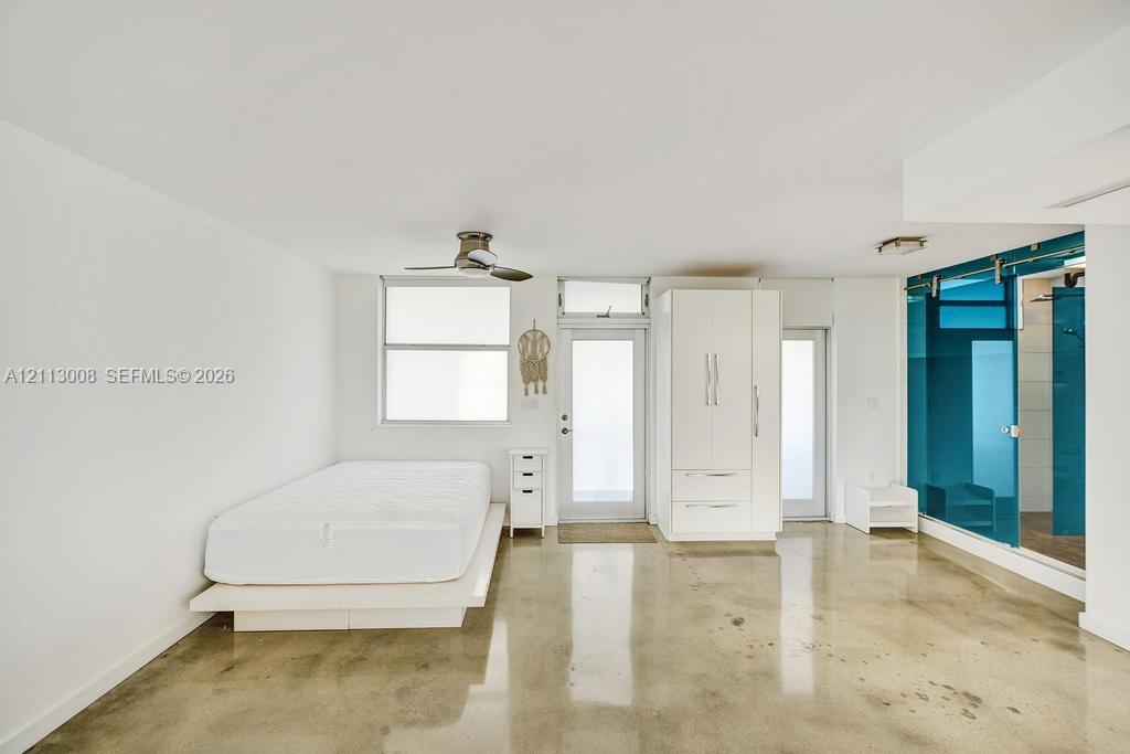 Polished concrete flooring, built-in white wardrobe cabinetry, ceiling fan, and sliding glass panel partition