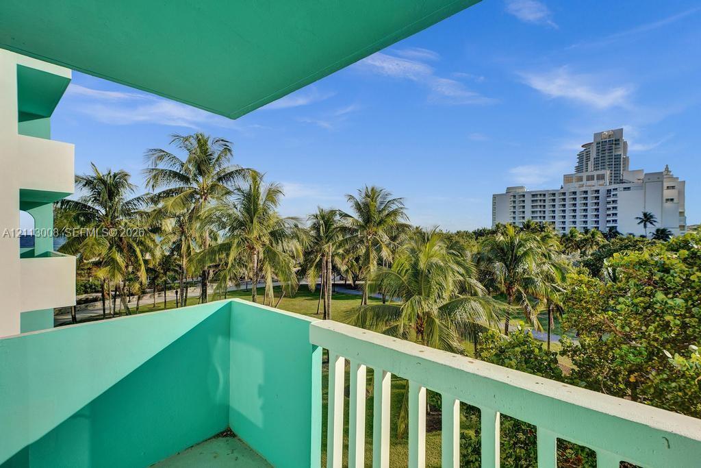 Outdoor balcony featuring a concrete railing and painted structural elements, overlooking a landscape of mature palm trees and green space