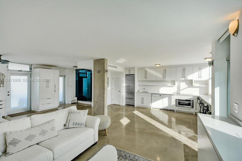 Open-concept interior featuring polished concrete flooring, white cabinetry, stainless steel appliances, and a central structural concrete pillar Open-concept interior featuring polished concrete flooring, white cabinetry, stainless steel appliances, and a central structural concrete pillar