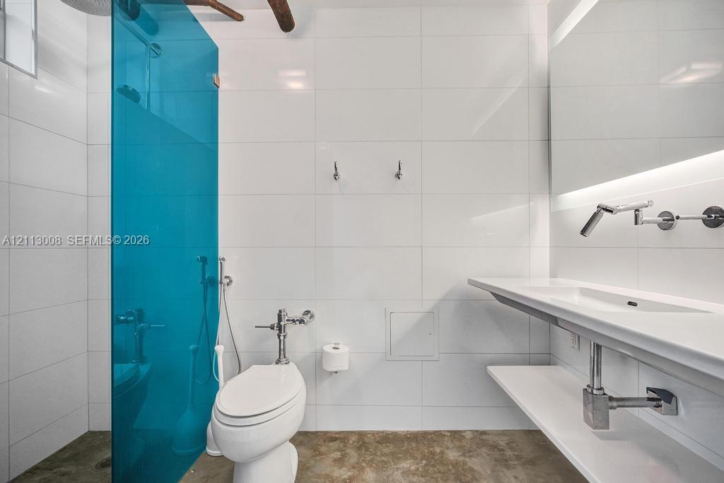 Bathroom featuring large-format white tile walls, a translucent blue glass shower partition, a wall-mounted floating vanity with integrated sink, and polished metal wall-mounted faucet hardware