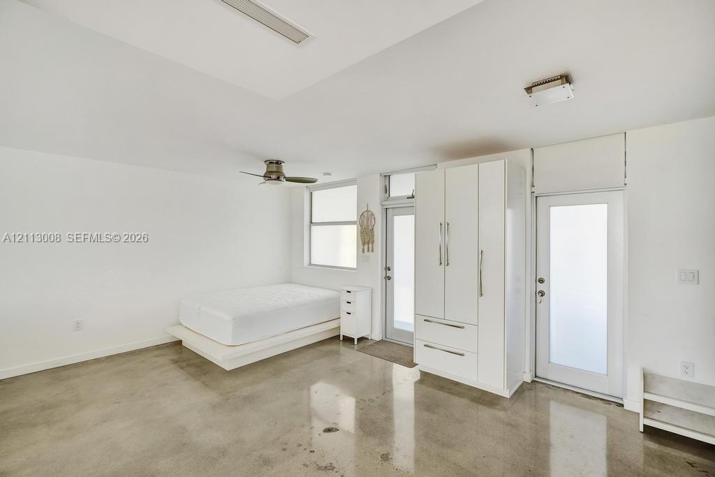 Polished concrete flooring, built-in white wardrobe cabinetry, ceiling fan, and frosted-glass panel doors