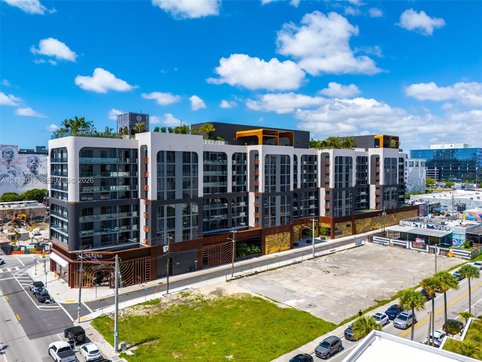 Multi-story architectural complex featuring a contemporary facade with integrated balconies, metallic exterior accents, ground-level retail frontage, and rooftop terrace space