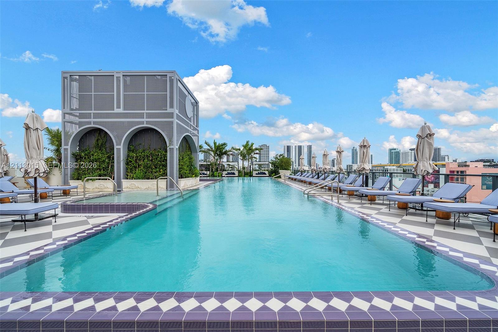 Rooftop swimming pool featuring geometric patterned tile decking, arched architectural cabana, integrated metal railing, and decorative tiled coping