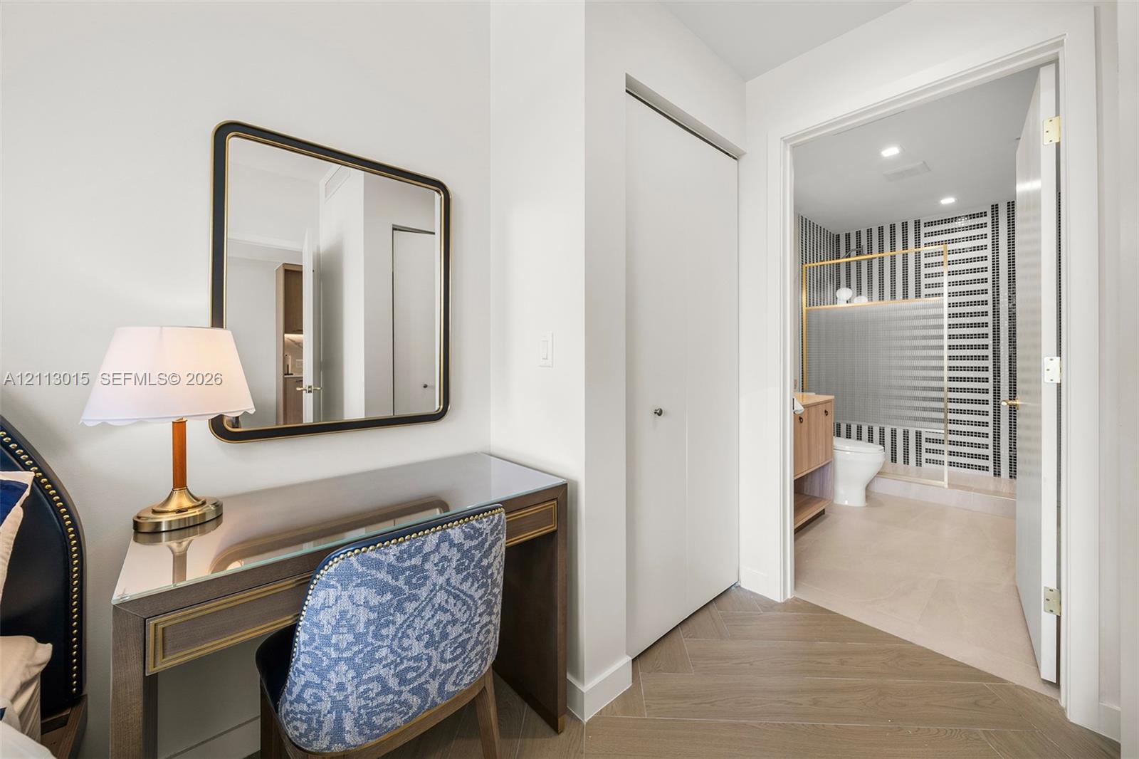 Wood-finish flooring in a herringbone pattern, white interior doors, and a bathroom featuring a walk-in shower with gold-tone hardware and high-contrast vertical tile accents