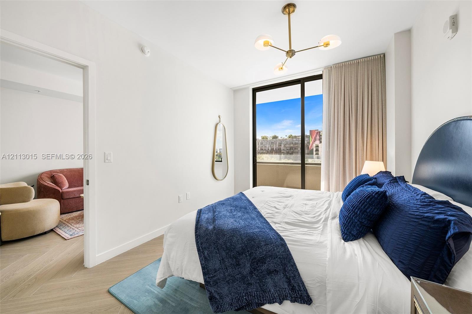 Bedroom featuring wood-finish flooring in a herringbone pattern, floor-to-ceiling glass sliding doors, a gold-toned multi-arm light fixture, and a balcony