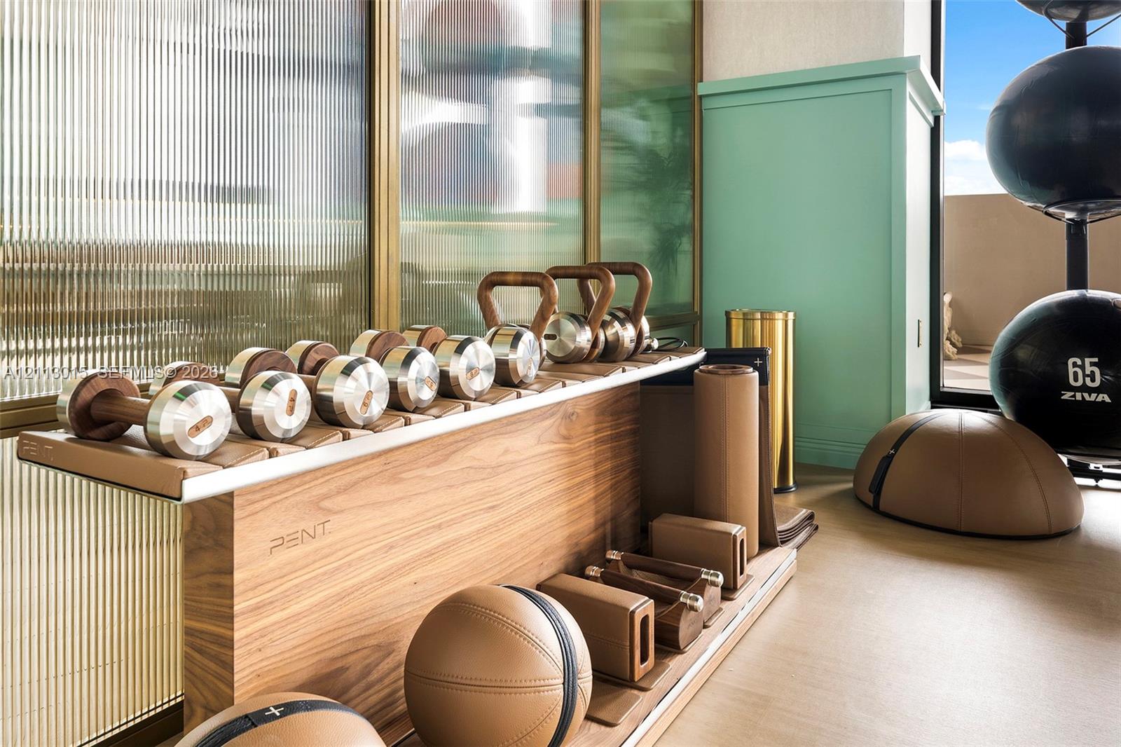 Custom wood-grain exercise equipment rack featuring metallic accents, ribbed glass wall paneling with brass-tone framing, and a floor-to-ceiling built-in mint green storage cabinet