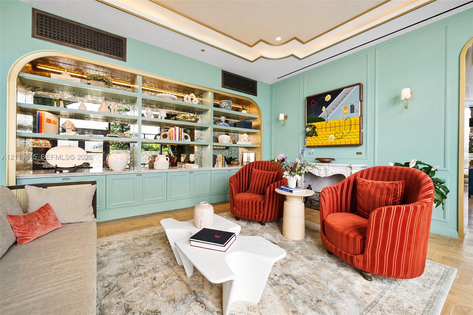 Custom built-in arched shelving featuring mirrored backing and recessed lighting, ornate fireplace mantel, wall paneling details, and tray ceiling with stepped gold-tone molding