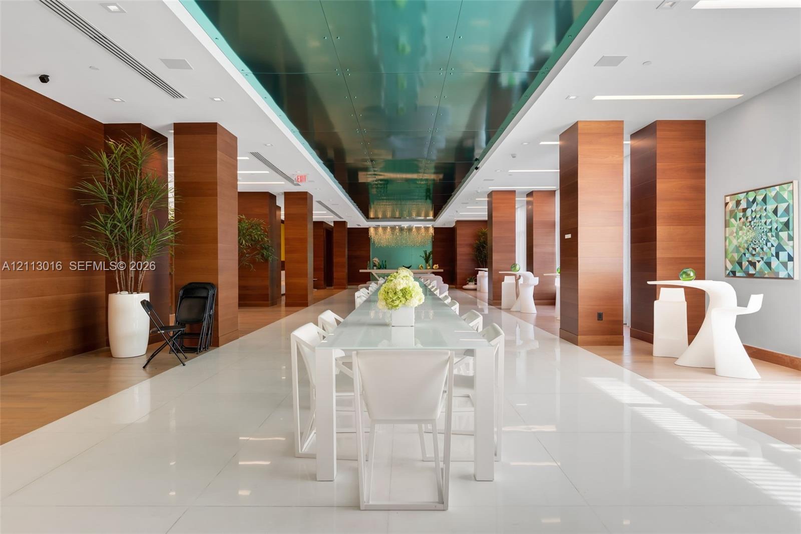 Expansive hall featuring polished tile flooring, floor-to-ceiling wood-panel columns, a high-gloss teal reflective ceiling, and recessed linear lighting