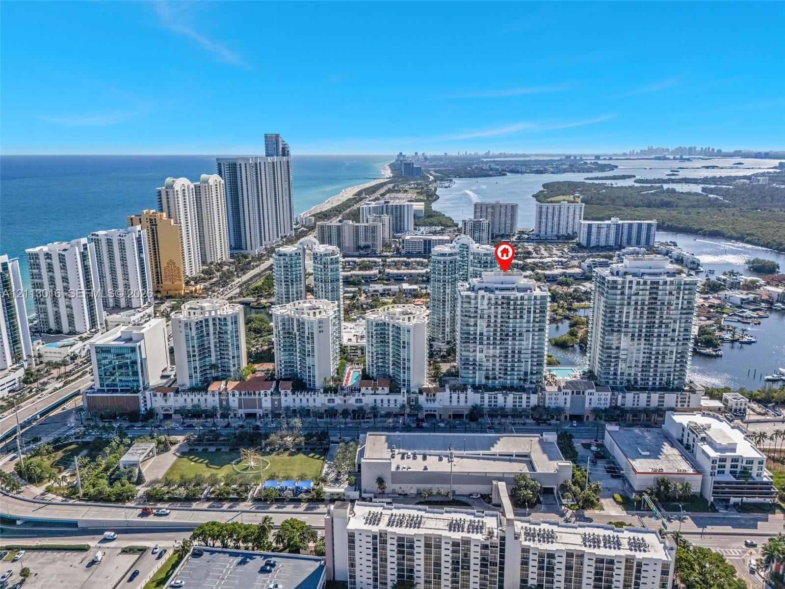 Aerial perspective of a high-rise residential structure positioned on the coast, featuring proximity to waterfront areas and surrounding urban development