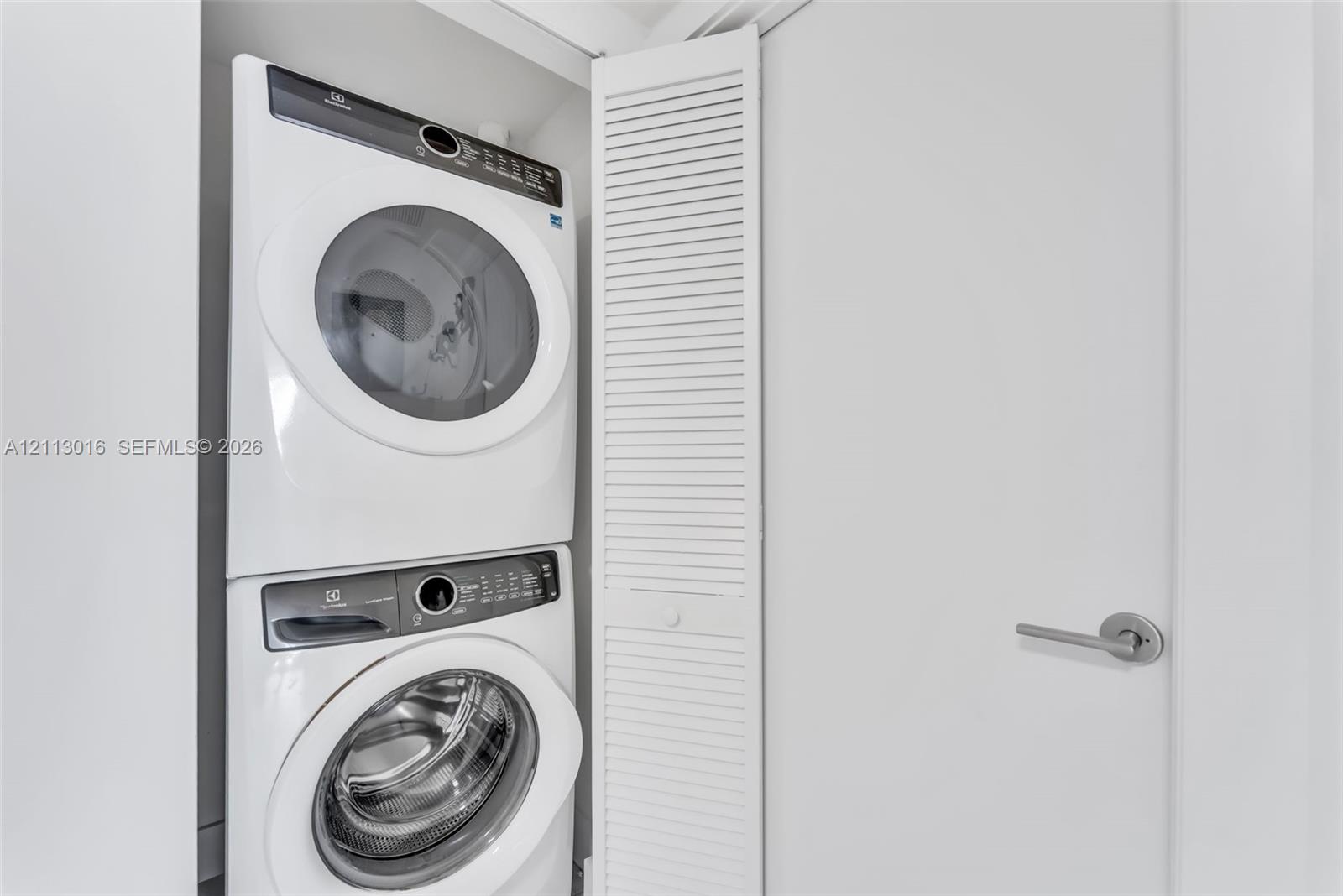 Stacked white front-load washer and dryer set enclosed within a white louvered-door closet Stacked white front-load washer and dryer set enclosed within a white louvered-door closet
