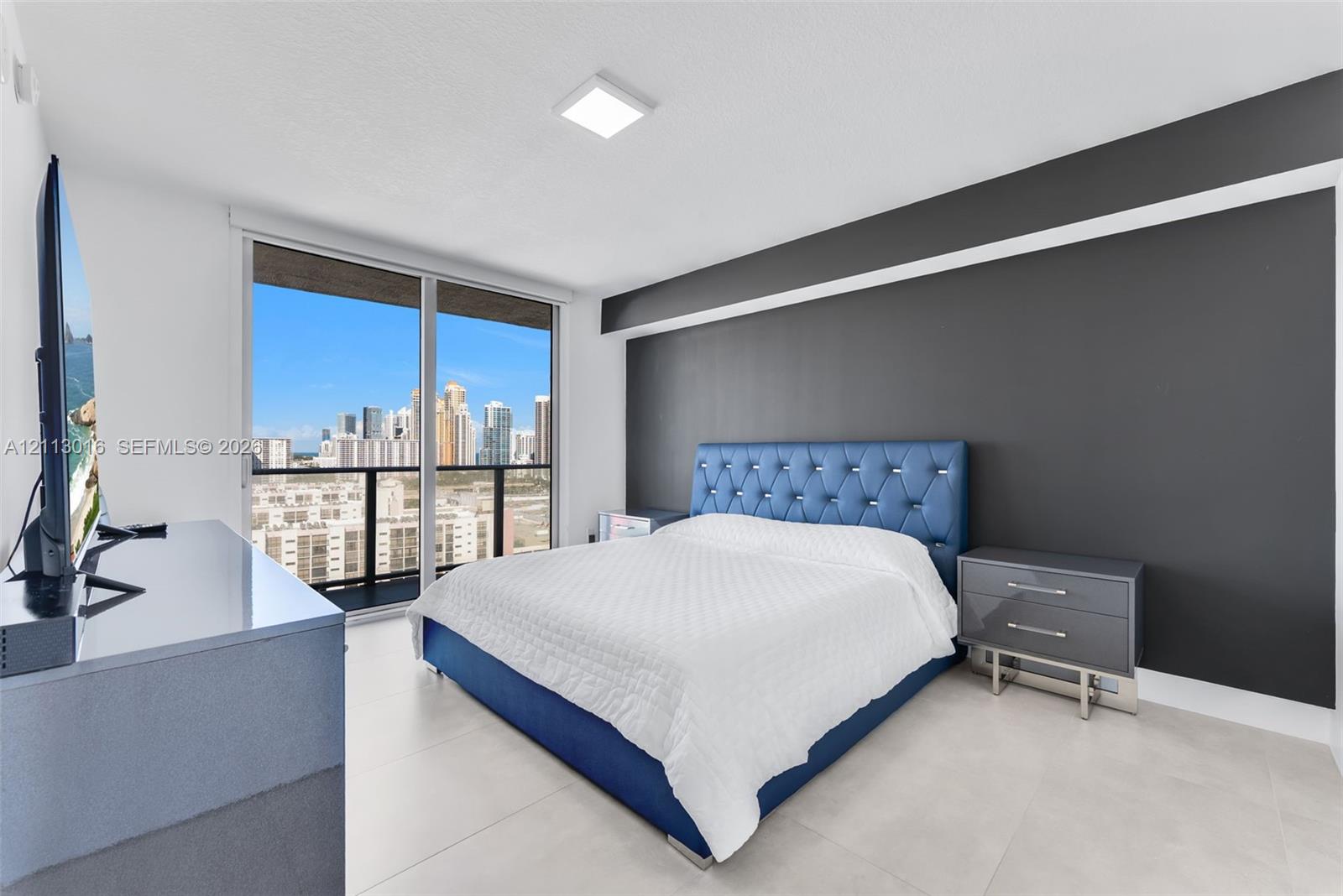 Floor-to-ceiling glass sliding doors, private balcony, neutral large-format tile flooring, and dark-toned accent wall