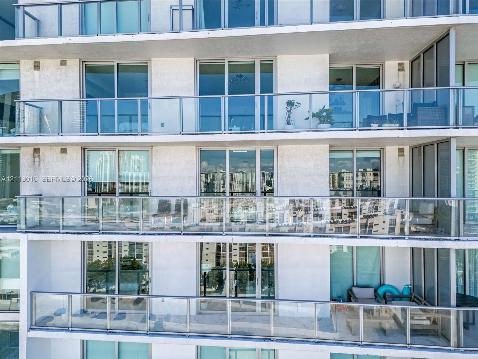 Multi-story concrete exterior featuring full-height glass sliding doors and private balconies with transparent glass railings