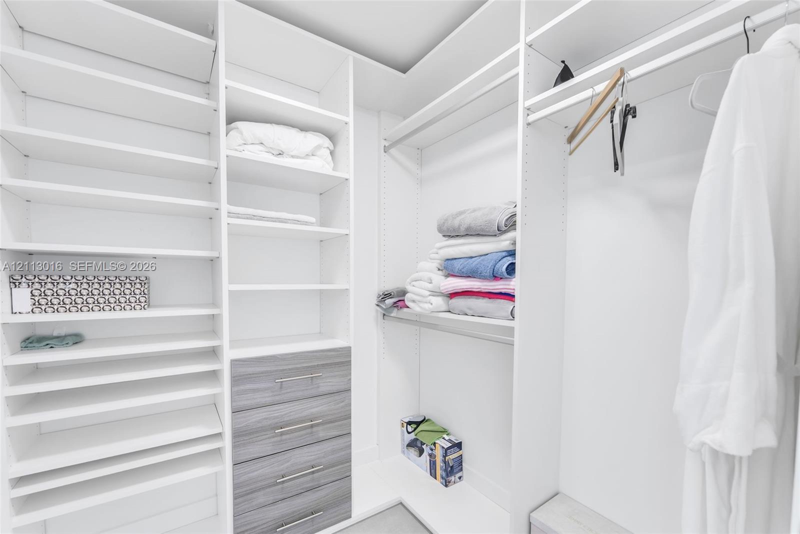 Walk-in closet featuring extensive built-in white shelving, integrated hanging rods, and a four-drawer dresser unit with wood-finish drawer fronts and metal pulls