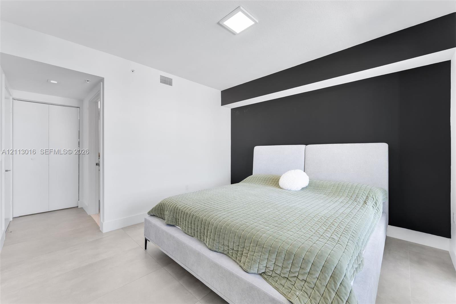 Neutral tile flooring, matte black accent wall, and recessed ceiling lighting