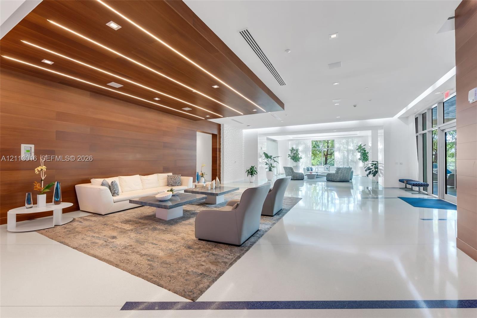 Interior common area featuring smooth polished flooring, wood-paneled accent wall, recessed linear lighting, and floor-to-ceiling glass entry doors