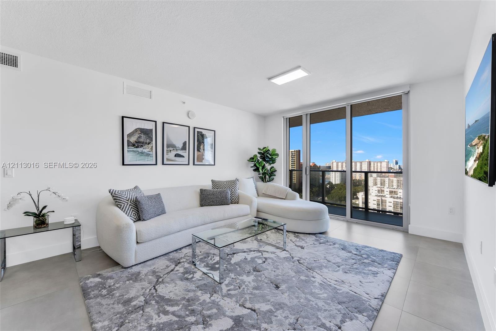 Living area featuring large-format tile flooring, floor-to-ceiling glass panel windows, and a black metal balcony railing Living area featuring large-format tile flooring, floor-to-ceiling glass panel windows, and a black metal balcony railing