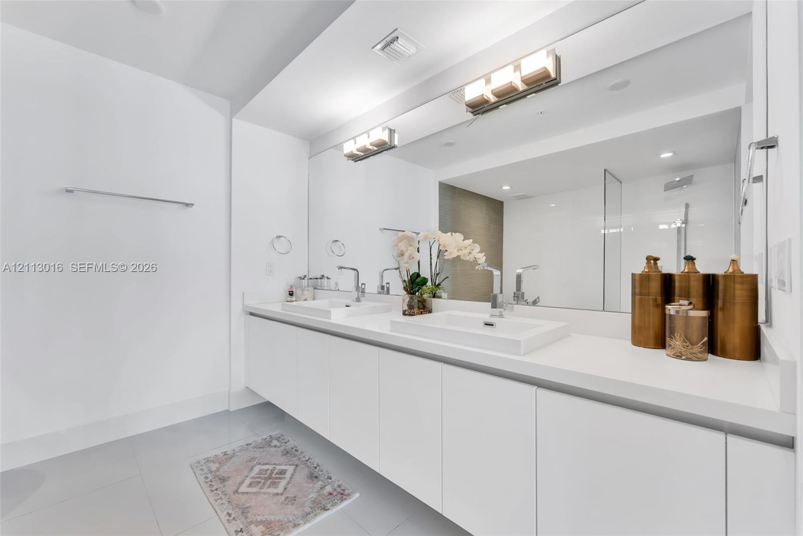 Floating double vanity featuring rectangular vessel sinks, white countertop, oversized wall-to-wall mirror, and dual multi-light fixtures