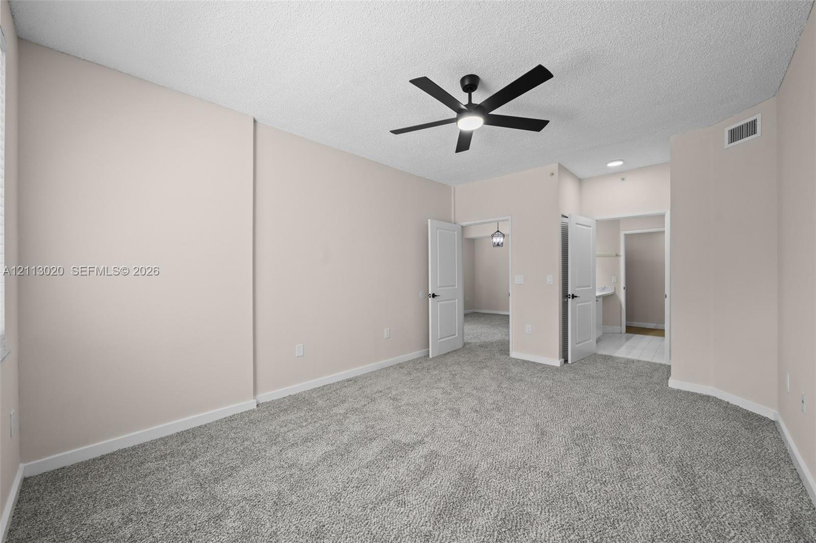 Neutral-toned interior space featuring textured carpeted flooring, a ceiling fan with integrated lighting, and white six-panel interior doors