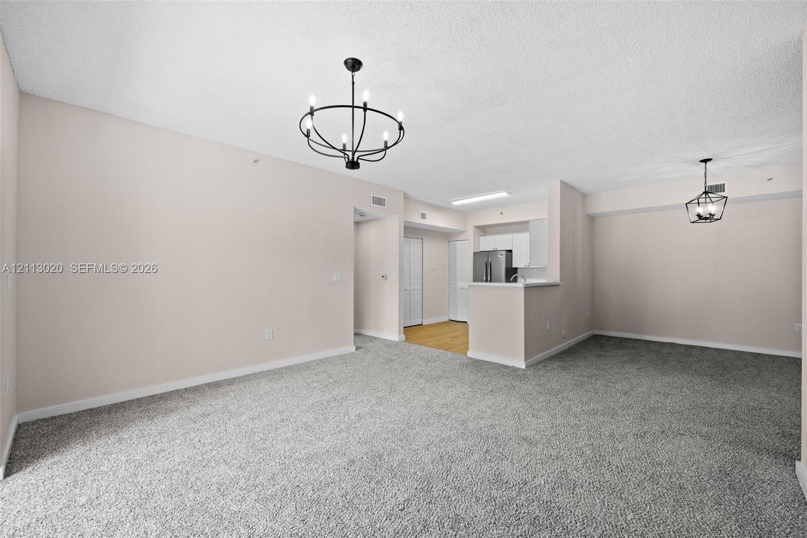 Open-concept interior featuring neutral wall tones, wall-to-wall carpeting, and two black-finished geometric chandeliers