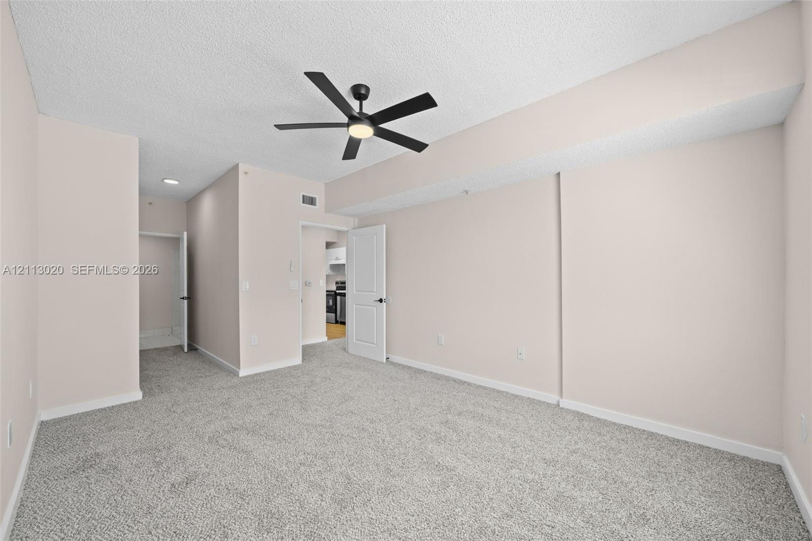 Neutral-toned interior space featuring wall-to-wall carpeting, a multi-blade ceiling fan with integrated lighting, and white paneled doors