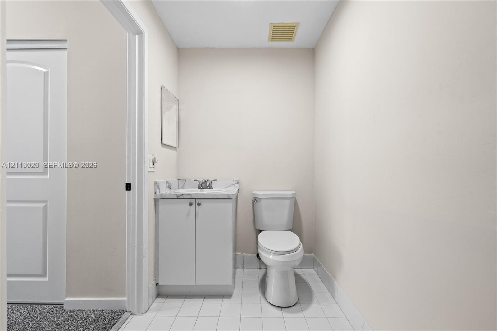 Vanity featuring a stone-patterned countertop and undermount sink, white cabinetry, porcelain-style floor tiling, and a standard-height toilet