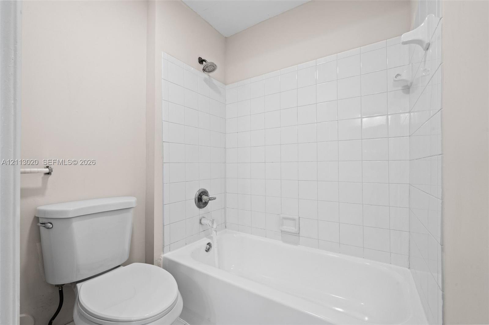 Full-size bathtub with white tile surround, integrated soap dish, and wall-mounted shower fixture, paired with a standard-height porcelain toilet