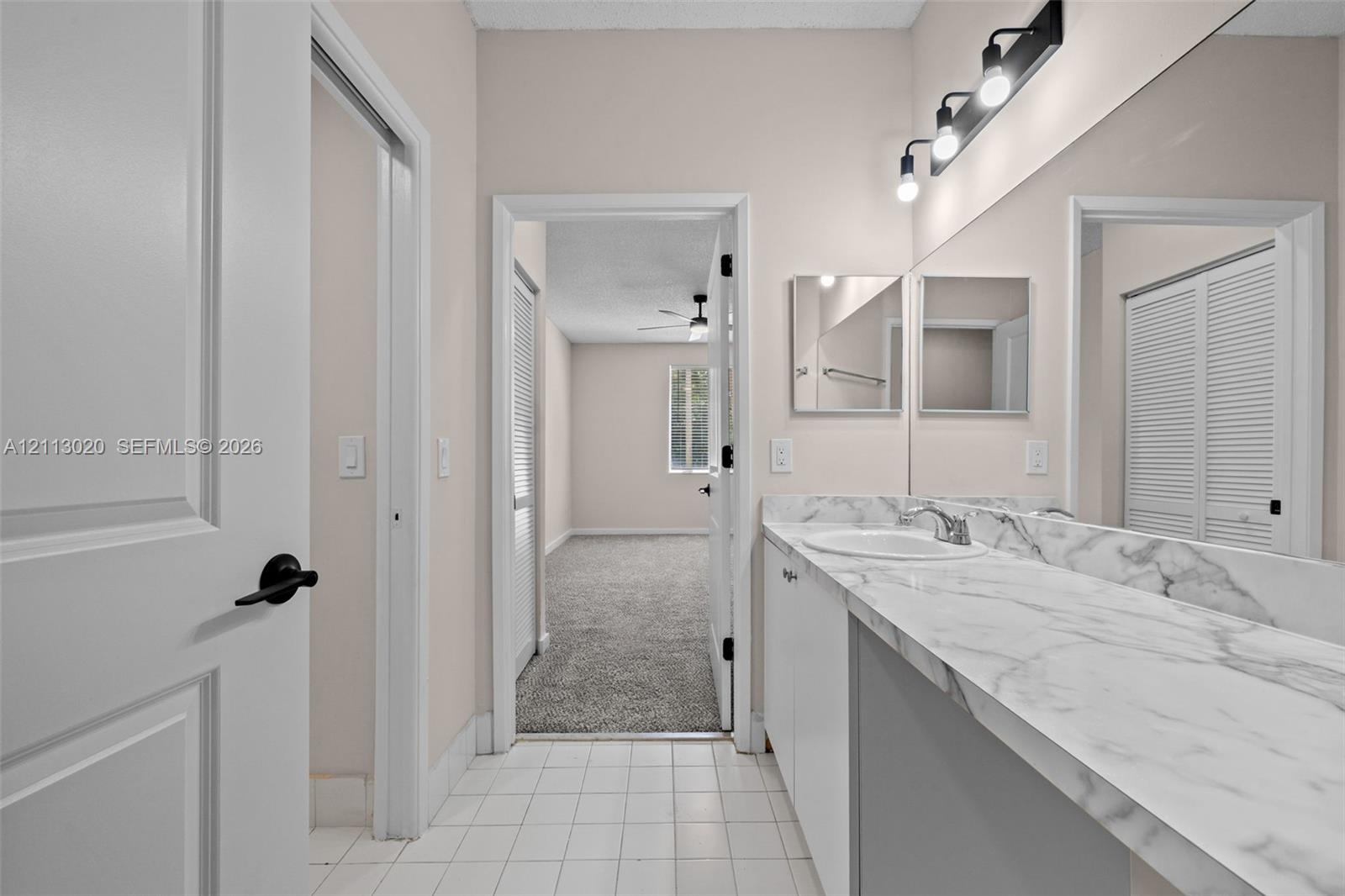Bathroom featuring a white vanity with stone-finish countertop, undermount sink, full-width mirror, and multi-bulb vanity lighting