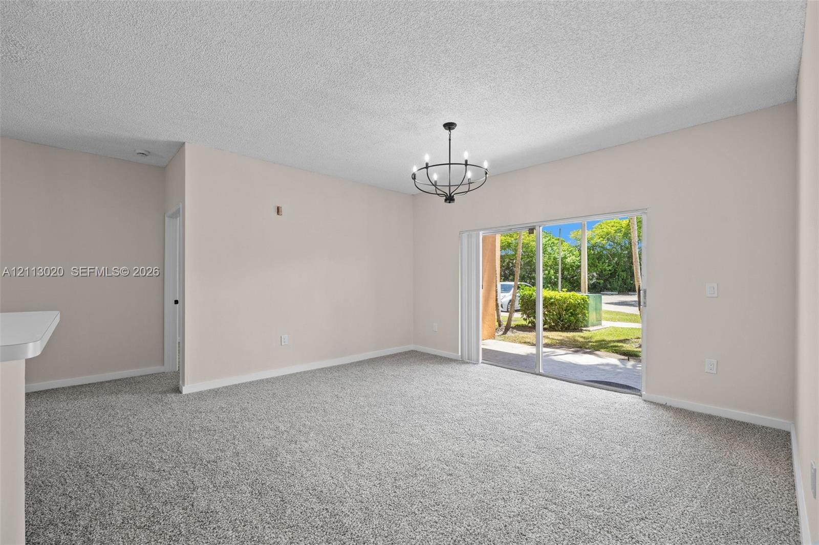 Neutral-toned interior featuring carpeting, a metal multi-light chandelier, and sliding glass doors