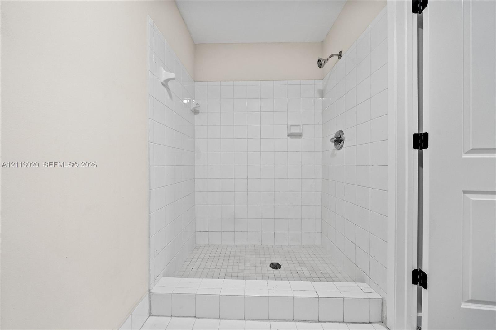 Walk-in shower featuring white square-tile surround, tile-finished curb, integrated soap niche, wall-mounted shower head, and chrome fixtures