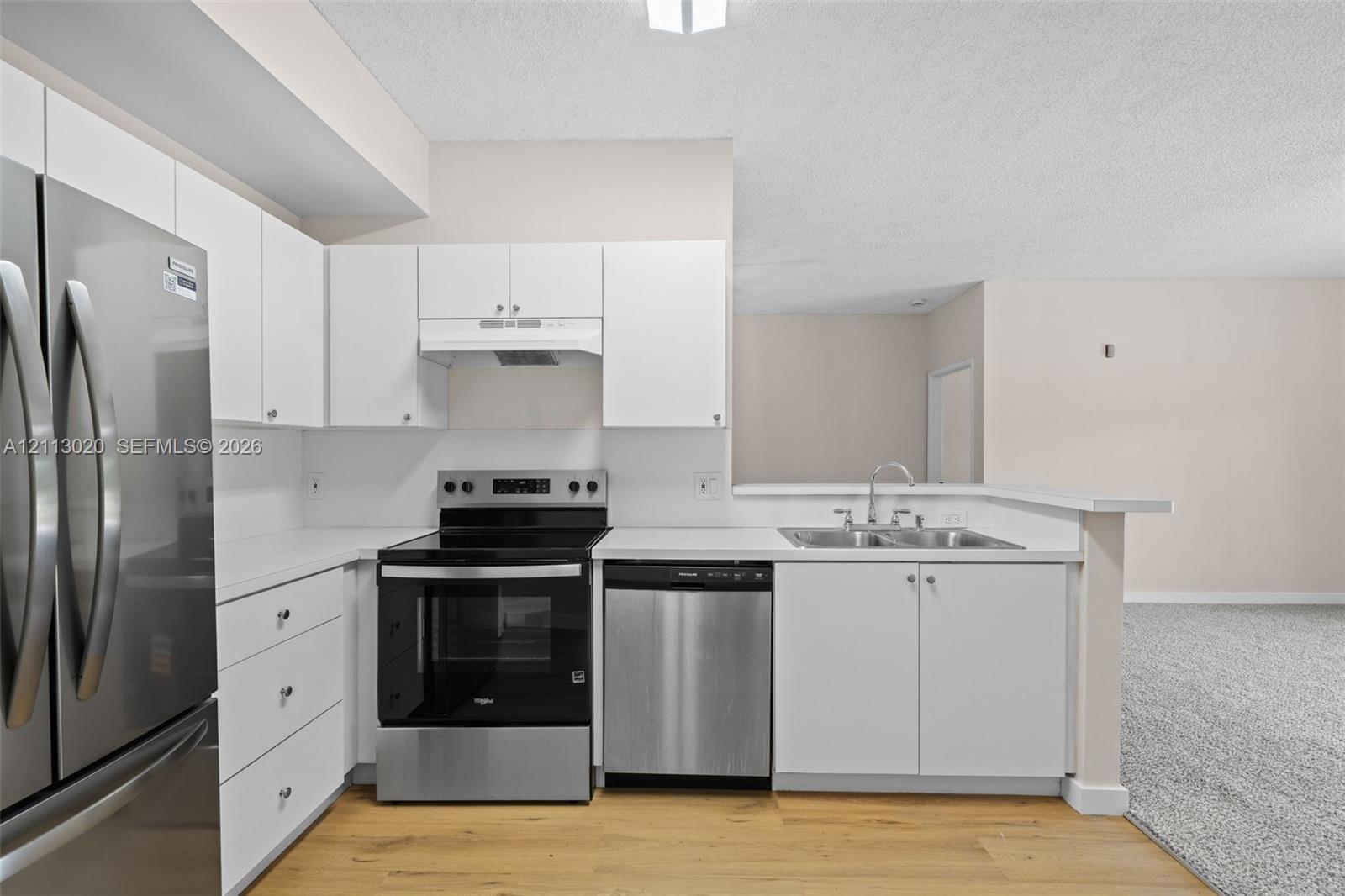 Kitchen featuring white cabinetry, solid-surface countertops, stainless steel appliances, a double-basin sink, and wood-finish flooring