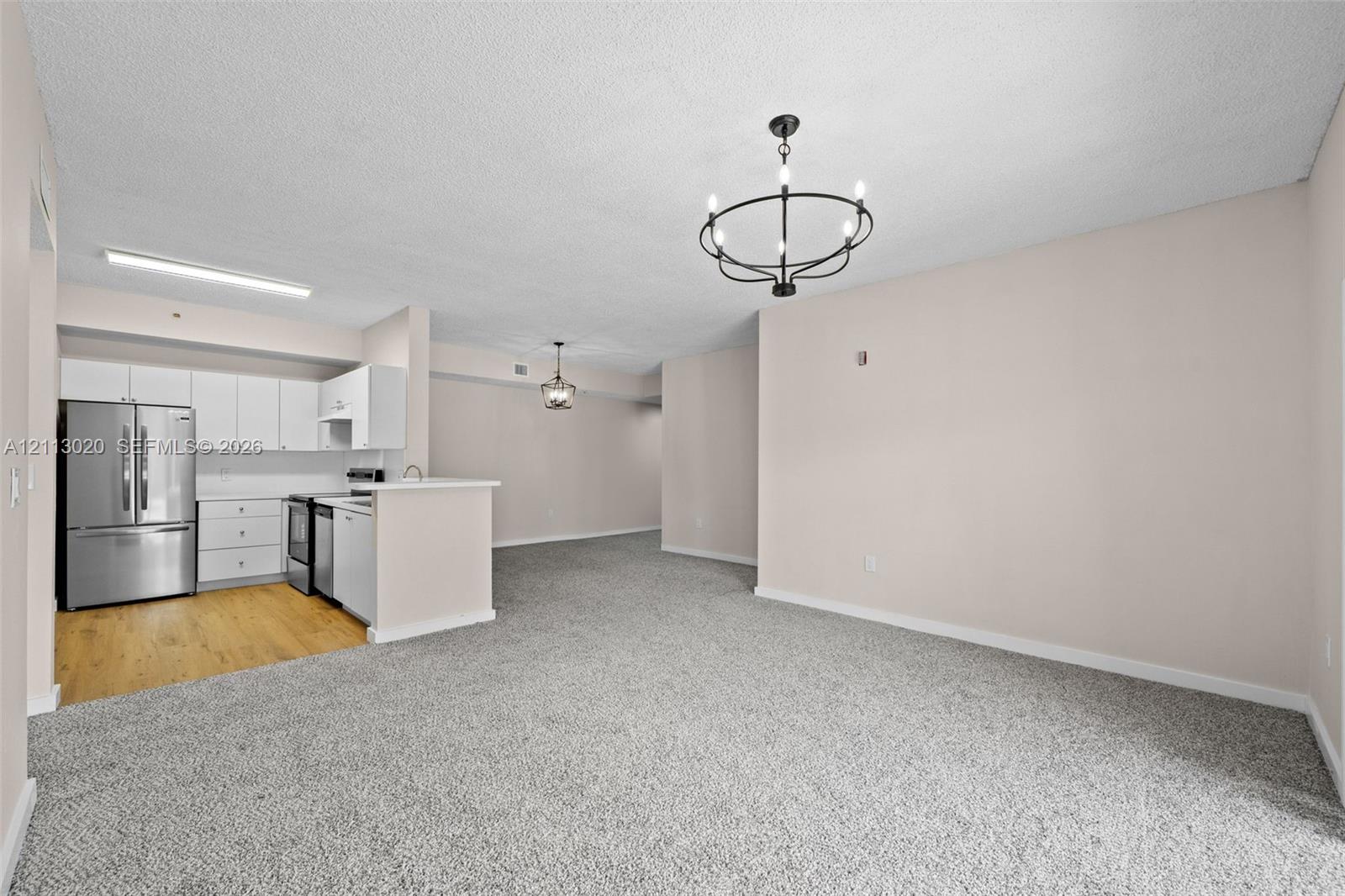 Kitchen featuring white cabinetry, stainless steel refrigerator, and wood-finish flooring, complemented by a matte black circular chandelier and neutral carpeting